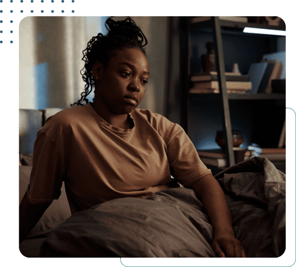 Person sitting on bed, looking contemplative.