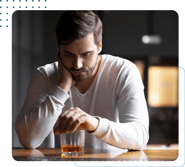 Man seated, looking at glass of whiskey.